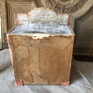 May include: A vintage cardboard box with a decorative top and a worn, brown exterior. The box has a rectangular shape and is slightly faded.