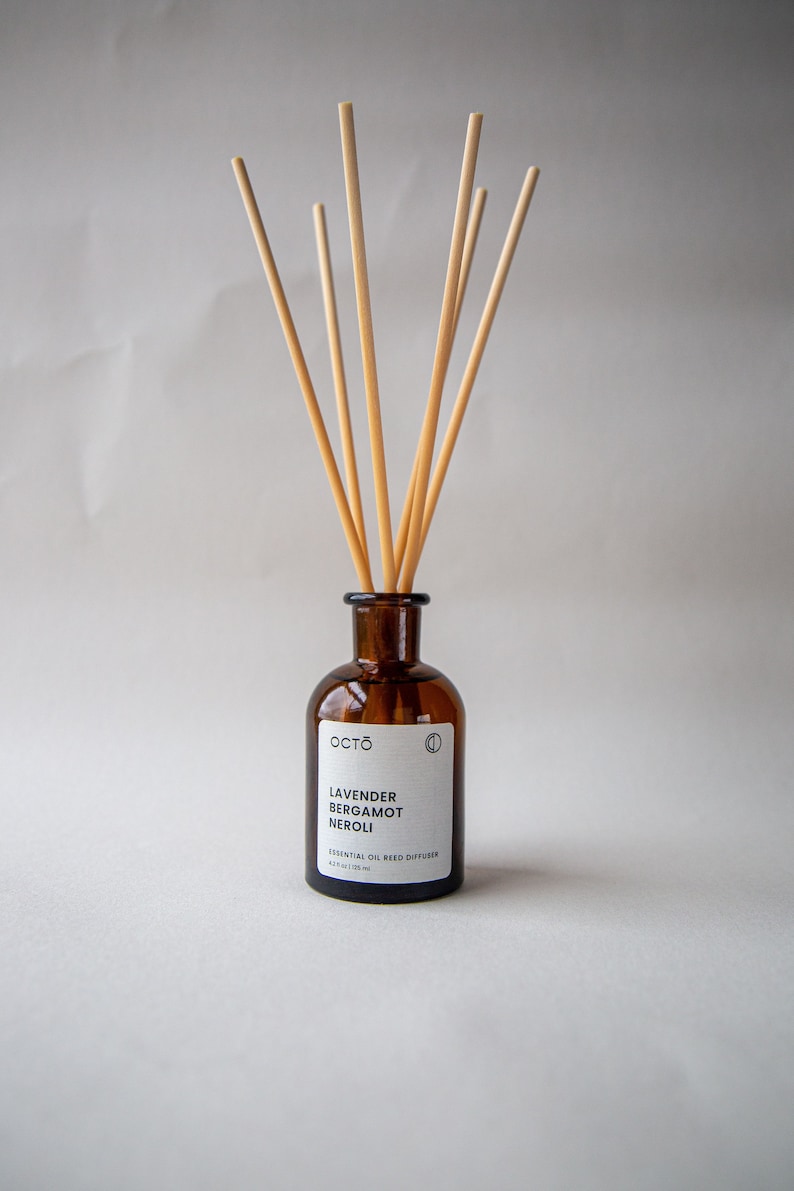 May include: A brown glass bottle with a white label that reads "OCTO Lavender Bergamot Neroli Essential Oil Reed Diffuser 4.2 fl oz / 125 ml". The bottle has wooden sticks sticking out of the top.