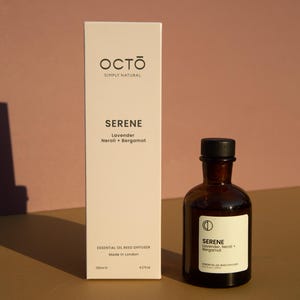 May include: A white box with the text "OCTO SIMPLY NATURAL" and "SERENE Lavender Neroli + Bergamot" on it. The box is next to a brown glass bottle with a black lid. The bottle has the text "SERENE Lavender, Neroli + Bergamot" on it. The bottle is labeled "ESSENTIAL OIL REED DIFFUSER 4.2 oz (125ml)".