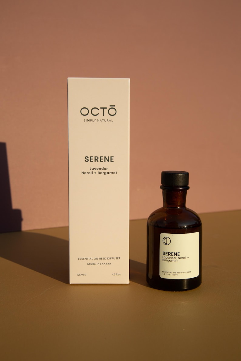 May include: A white box with the text "OCTO SIMPLY NATURAL" and "SERENE Lavender Neroli + Bergamot" on it. The box is next to a brown glass bottle with a black lid. The bottle has the text "SERENE Lavender, Neroli + Bergamot" on it. The bottle is labeled "ESSENTIAL OIL REED DIFFUSER 4.2 oz (125ml)".