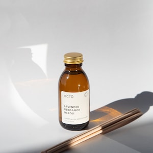 May include: A brown glass bottle with a gold lid and a white label that reads "Octo Lavender Bergamot Neroli Essential Oil Reed Diffuser 4.2 fl oz / 120 ml". The bottle is sitting on a white surface with a set of wooden diffuser sticks.
