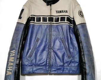 May include: A blue and white leather motorcycle jacket with black accents. The jacket has a zip fastening and two pockets on the front. The word "YAMAHA" is printed on the front of the jacket.