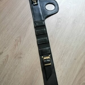 Puede incluir: Cintur&oacute;n de cuero negro con hebilla y un lazo. El cintur&oacute;n tiene una serie de ranuras verticales en la parte delantera.