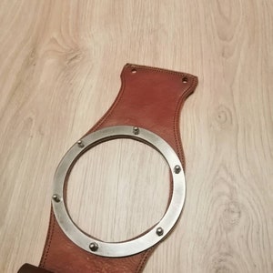 May include: A brown leather motorcycle sissy bar with a metal ring and rivets. The sissy bar has a brown leather pouch attached to the bottom.