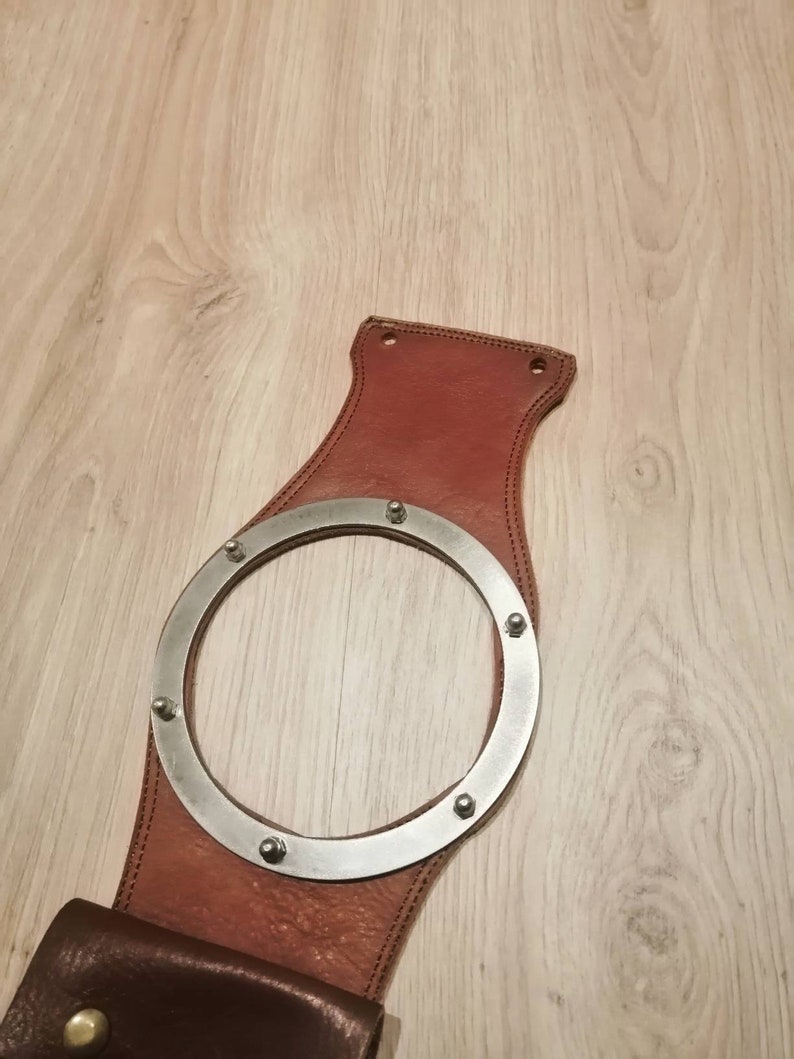 May include: A brown leather motorcycle sissy bar with a metal ring and rivets. The sissy bar has a brown leather pouch attached to the bottom.