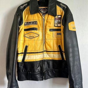 May include: A yellow and black leather jacket with a racing theme. The jacket has several patches, including "Redskins", "Goodyear Tires", "Castrol GTX Motor Oil", and "Brakes".