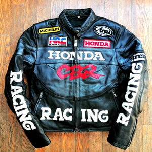 Könnte beinhalten: Schwarze Leder-Rennjacke mit "HONDA CBR" und "RACING" Grafiken in Weiß und Rot. Mit Aufnähern von Michelin, HRC Honda Racing und Arai. Die Jacke hat einen Reißverschluss vorne und ein klassisches Motorradjacken-Design.