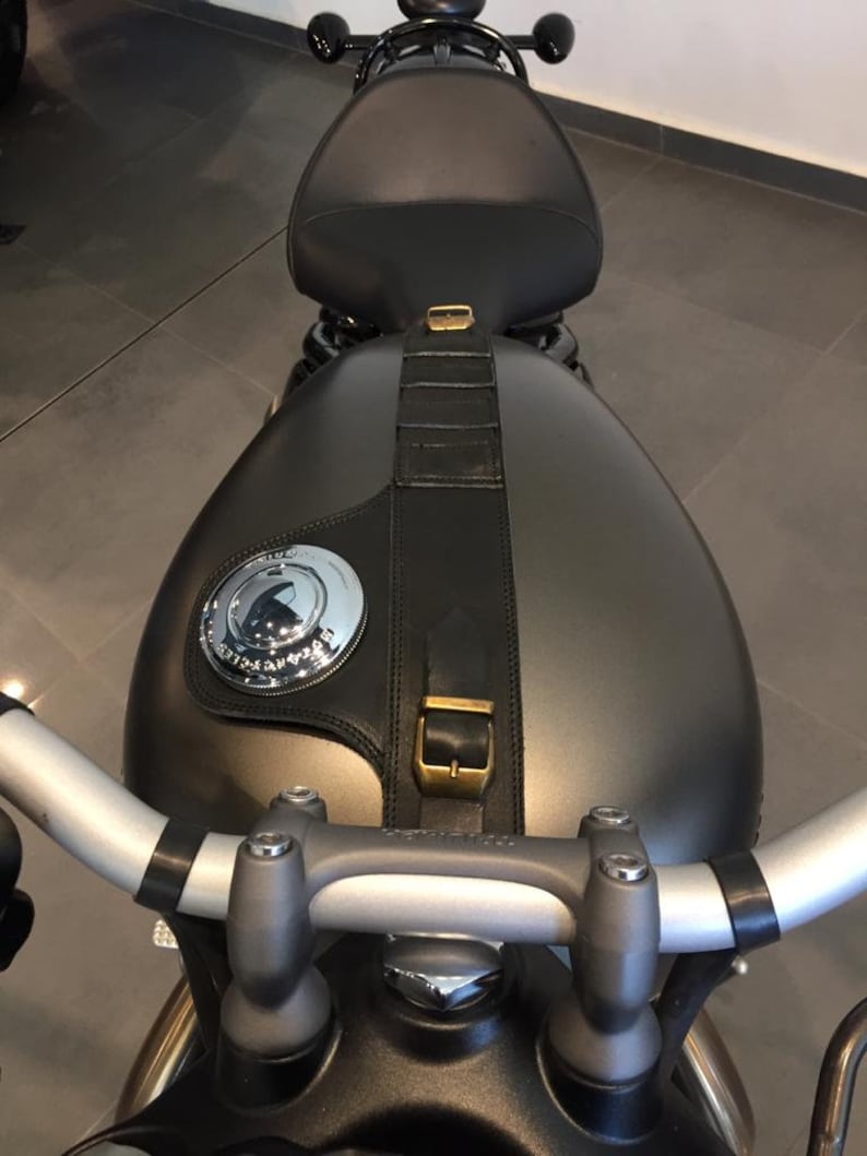 Puede incluir: Una motocicleta negra con un tanque de gasolina gris y un asiento de cuero negro. La motocicleta tiene un manillar plateado y una correa de cuero negro con una hebilla de lat&oacute;n.