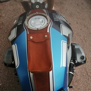 May include: A blue and silver motorcycle gas tank with a brown leather strap and a round metal gas cap with the text "OPTION" on it.