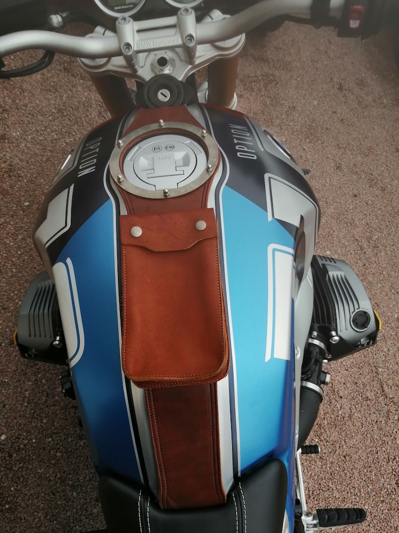May include: A blue and silver motorcycle gas tank with a brown leather strap and a round metal gas cap with the text "OPTION" on it.