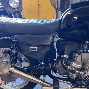 May include: A black motorcycle with a black leather saddlebag and a chrome exhaust pipe. The motorcycle has a black seat and a black engine. The motorcycle is parked in a garage.