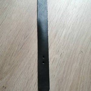 Puede incluir: Una correa de cuero negra con dos agujeros cerca del extremo, que se estrecha hasta un punto.