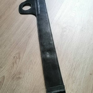 Puede incluir: Correa de guitarra de cuero negro con un asa de bucle. La correa es larga y estrecha, con un borde cosido.