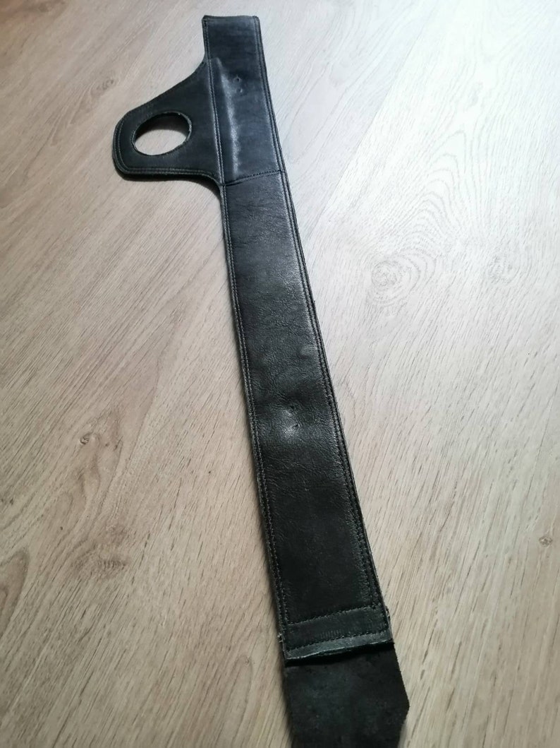 Puede incluir: Correa de guitarra de cuero negro con un asa de bucle. La correa es larga y estrecha, con un borde cosido.