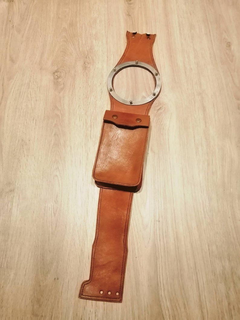 May include: A brown leather belt with a metal ring and a leather pouch. The belt is designed to be worn around the waist and has a metal ring that can be used to attach a key chain or other accessories. The pouch is attached to the belt and can be used to carry small items.