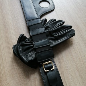 Puede incluir: Cintur&oacute;n de cuero negro con hebilla y una correa con m&uacute;ltiples ranuras. El cintur&oacute;n se combina con un par de guantes de cuero negro.