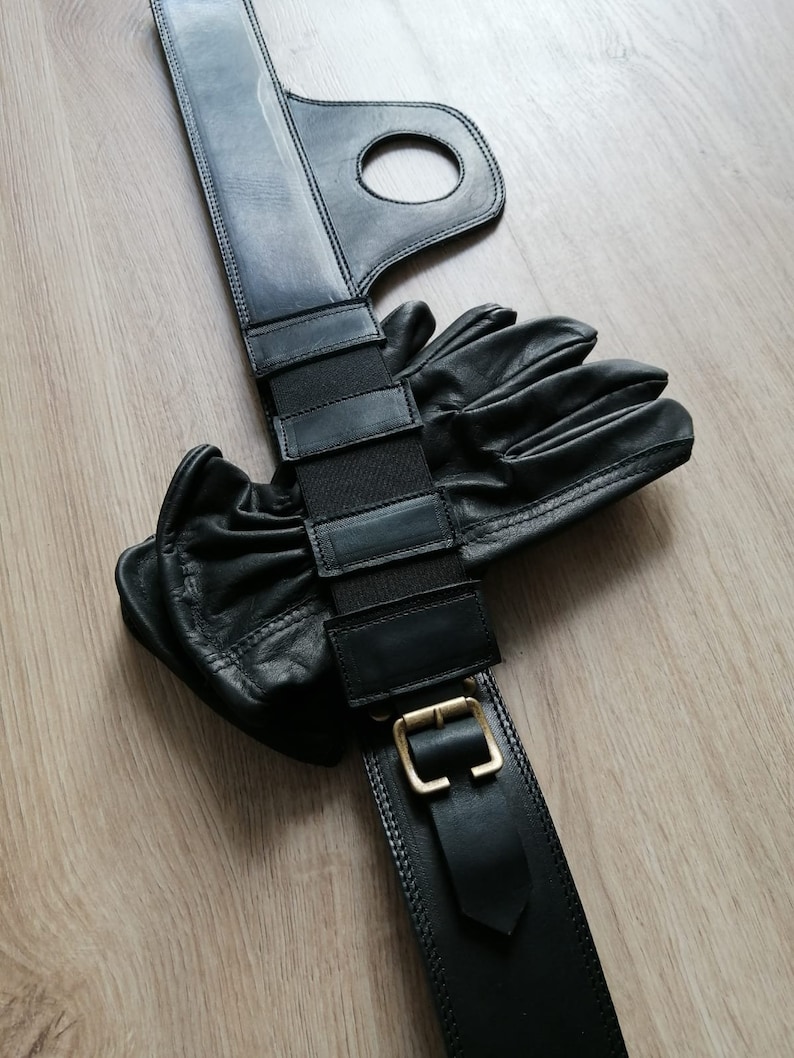 Puede incluir: Cintur&oacute;n de cuero negro con hebilla y una correa con m&uacute;ltiples ranuras. El cintur&oacute;n se combina con un par de guantes de cuero negro.