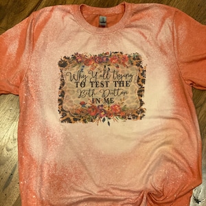 May include: Orange bleached t-shirt with a graphic print of a floral frame with the text "Why Y'all Trying To Test The Beth Dutton In Me".