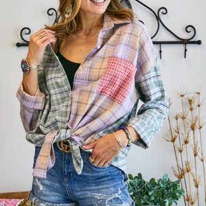 May include: A woman wearing a multi-colored plaid shirt tied at the waist with a gold belt, blue denim shorts, and round sunglasses.