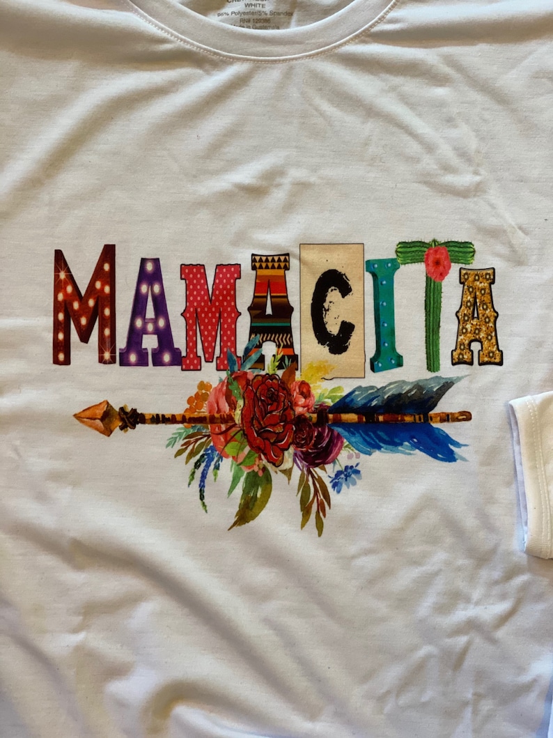 K&ouml;nnte beinhalten: Wei&szlig;es T-Shirt mit einem bunten Grafikdesign, das "Mamacita" mit einem floralen Pfeil-Design sagt.
