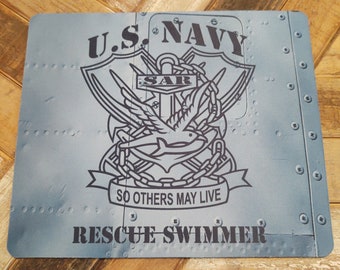 Może przedstawiać: Podkładka pod mysz w kolorze niebieskim i białym z czarno-białym obrazkiem emblematu ratownika wodnego US Navy. Emblemat przedstawia kotwicę, ptaka i napis "SAR" oraz "So Others May Live". Pod emblematem znajduje się napis "Rescue Swimmer".