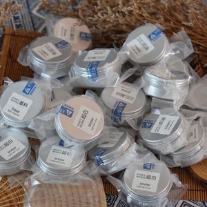 May include: A collection of small, silver, round containers with white lids. The containers are labeled with the words "Snow", "Base", "Cream", and "超白".