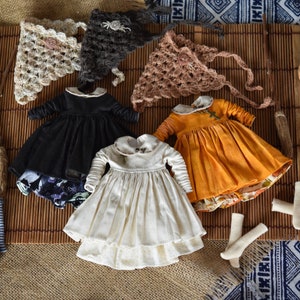 Può includere: Tre abiti da bambola in nero, bianco e giallo con cappelli all'uncinetto in marrone, beige e grigio. Gli abiti hanno diversi motivi e trame. I cappelli sono tutti di forma triangolare.