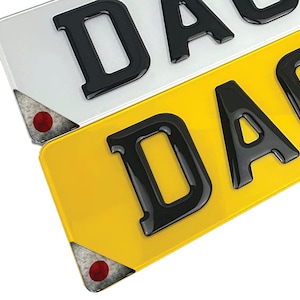 May include: Two license plates with the word "DAB" printed in black 3D letters on a yellow and white background. The plates have reflective corners.