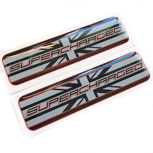 May include: Two black and silver decals with a red outline. The decals feature a Union Jack flag design and the text "SUPERCHARGED".