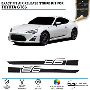 Puede incluir: Toyota GT86 blanco con calcomanías de rayas negras y blancas. Las calcomanías presentan el número 86. La imagen muestra el coche de lado y de frente. La imagen también incluye un logotipo para Concept Graphics.