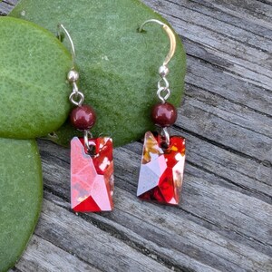 May include: Red and gold rectangular crystal earrings with maroon beads hanging from silver hooks.