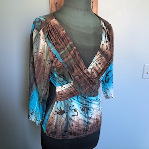 May include: A brown and blue patterned blouse with a V-neck and 3/4 sleeves. The blouse has a criss-cross design in the front.