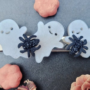 May include: Three white ghost-shaped hair clips with black glitter spiders. The ghosts have a smiling face and are translucent.