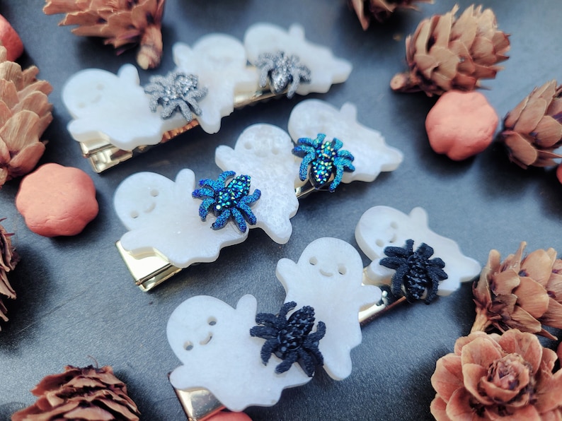 May include: Set of six white ghost hair clips with sparkly blue and black spiders. The clips are perfect for Halloween.
