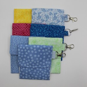 May include: Six fabric pouches with different patterns, including polka dots, stars, and geometric designs. Each pouch has a silver metal clip attached.