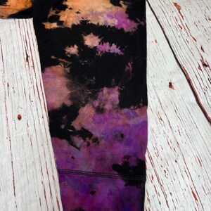 Op de afbeelding: Een zwart longsleeve shirt met een tie-dye patroon in tinten oranje, paars en zwart. Het shirt heeft een geribbelde manchet en is gemaakt van een zachte, comfortabele stof.