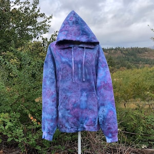 May include: A tie-dye hoodie in shades of blue and purple. The hoodie has a drawstring hood and a kangaroo pocket.