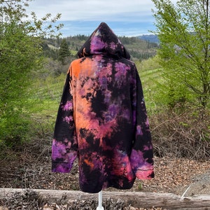 Op de afbeelding: Zwarte hoodie met een tie-dye patroon in tinten oranje, paars en roze.