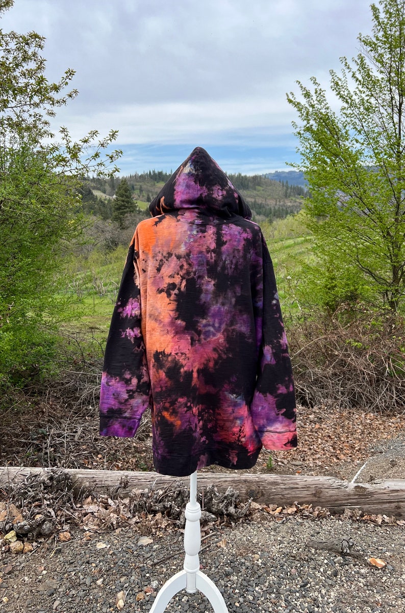 Op de afbeelding: Zwarte hoodie met een tie-dye patroon in tinten oranje, paars en roze.