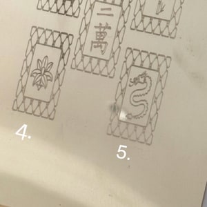 May include: A collection of five rectangular tiles with intricate designs. Each tile features a unique symbol or number, including wheels, bamboo stalks, and a dragon. The tiles are set against a light-colored background.