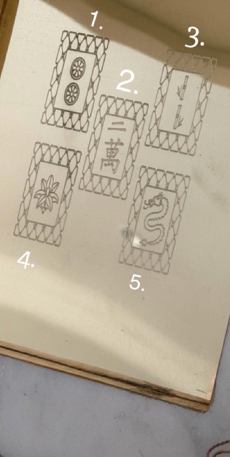 May include: A collection of five rectangular tiles with intricate designs. Each tile features a unique symbol or number, including wheels, bamboo stalks, and a dragon. The tiles are set against a light-colored background.