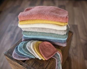 May include: A stack of knitted baby hats in various colors, including pink, yellow, white, green, blue, and gray. The hats are arranged in a pile on a wooden surface.
