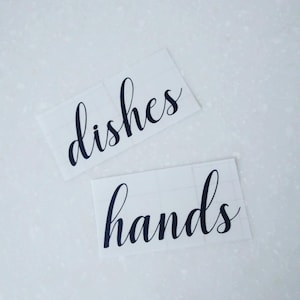 May include: Two white labels with black cursive text. The top label says "dishes" and the bottom label says "hands".