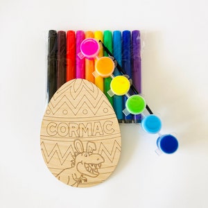 May include: Wooden Easter egg shaped craft with a dinosaur design and the name "CORMAC" written on it. The craft comes with a set of colorful markers and paint pots.