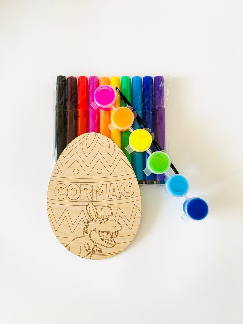 May include: Wooden Easter egg shaped craft with a dinosaur design and the name "CORMAC" written on it. The craft comes with a set of colorful markers and paint pots.