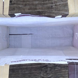 May include: An open, rectangular tote bag with a light-colored interior and a brown exterior. The bag has handles and reinforced corners. The interior is white, and the exterior has text and a purple polka-dot pattern.