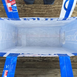 May include: A blue and white tote bag with blue handles. The bag is made from a recycled material and has text printed on the sides. The bag is empty and viewed from the inside.
