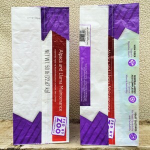 May include: Two feed bags for alpacas and llamas. The bags are white with purple and red accents. Text on the bags includes "Alpaca and Llama Maintenance" and "Net Wt. 50 lb (22.67 kg)". The bags are labeled "Fed by Zoo Professionals".