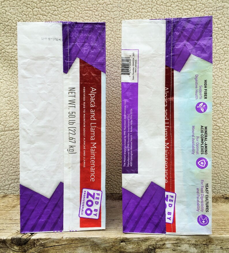 May include: Two feed bags for alpacas and llamas. The bags are white with purple and red accents. Text on the bags includes "Alpaca and Llama Maintenance" and "Net Wt. 50 lb (22.67 kg)". The bags are labeled "Fed by Zoo Professionals".