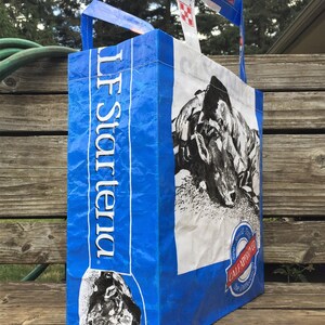 May include: A blue and white tote bag made from recycled material. The bag features a black and white image of a cow and the text "LF Star Tenda". The bag has handles for carrying.